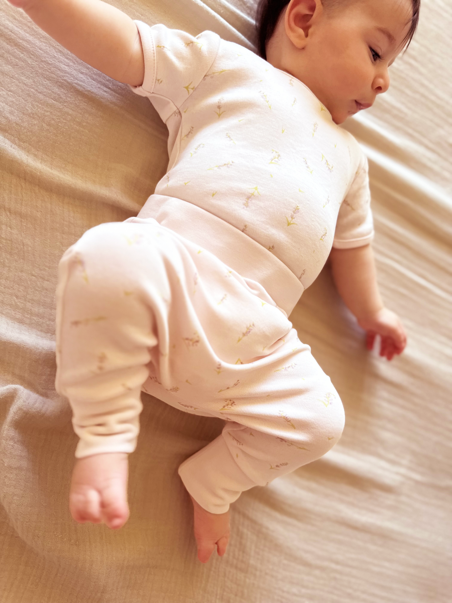 Baby in a pale pink outfit lying on a beige surface