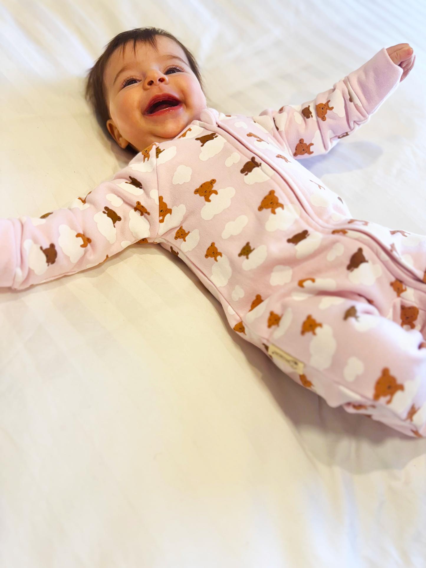 Baby in a pink outfit with brown bear patterns lying on a white surface