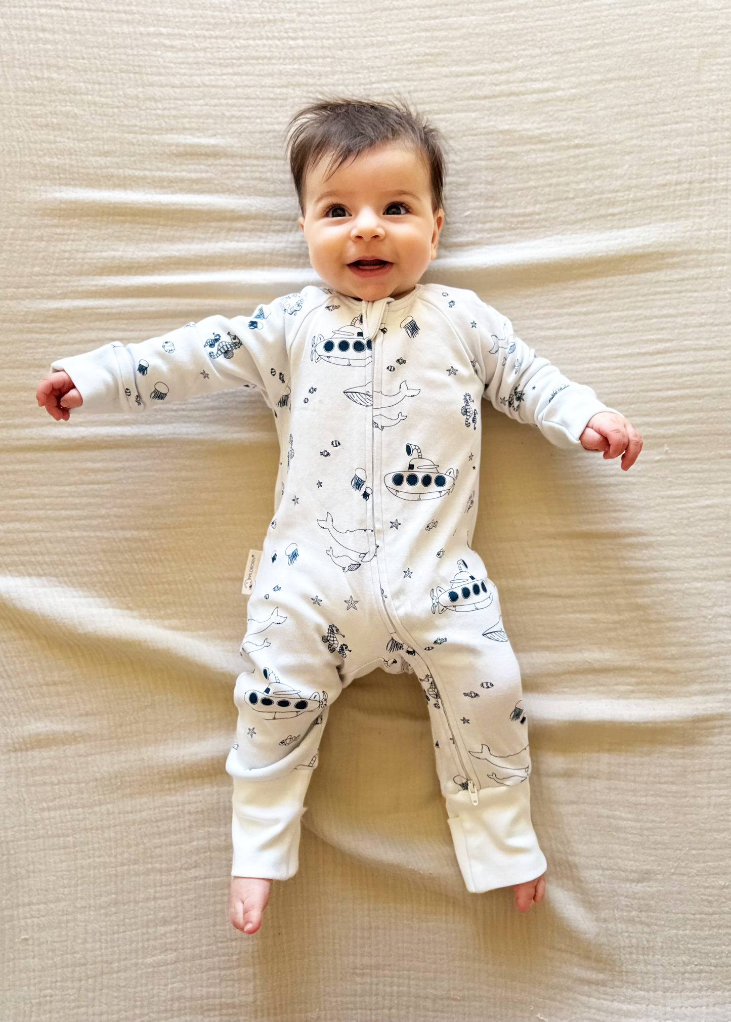 Baby wearing a white onesie with under water pattern on a beige textured surface