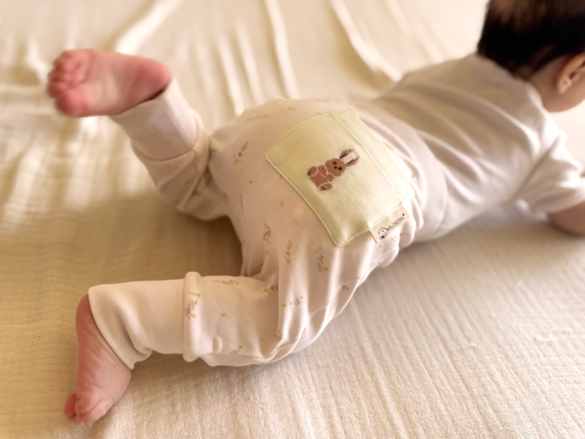 Baby wearing a pale pink outfit with a small bunny embroidery design on a light-colored surface