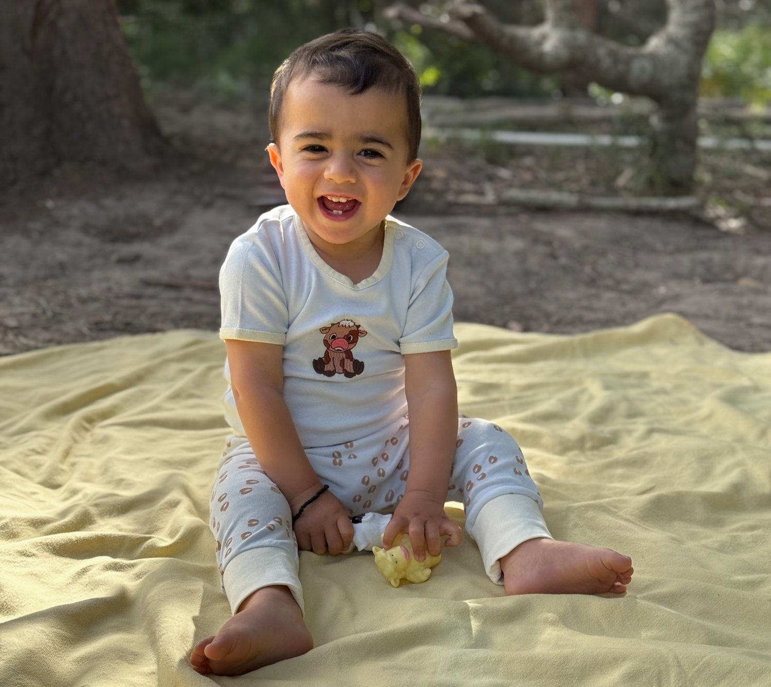 Child sitting on a yellow blanket outdoors with trees in the background