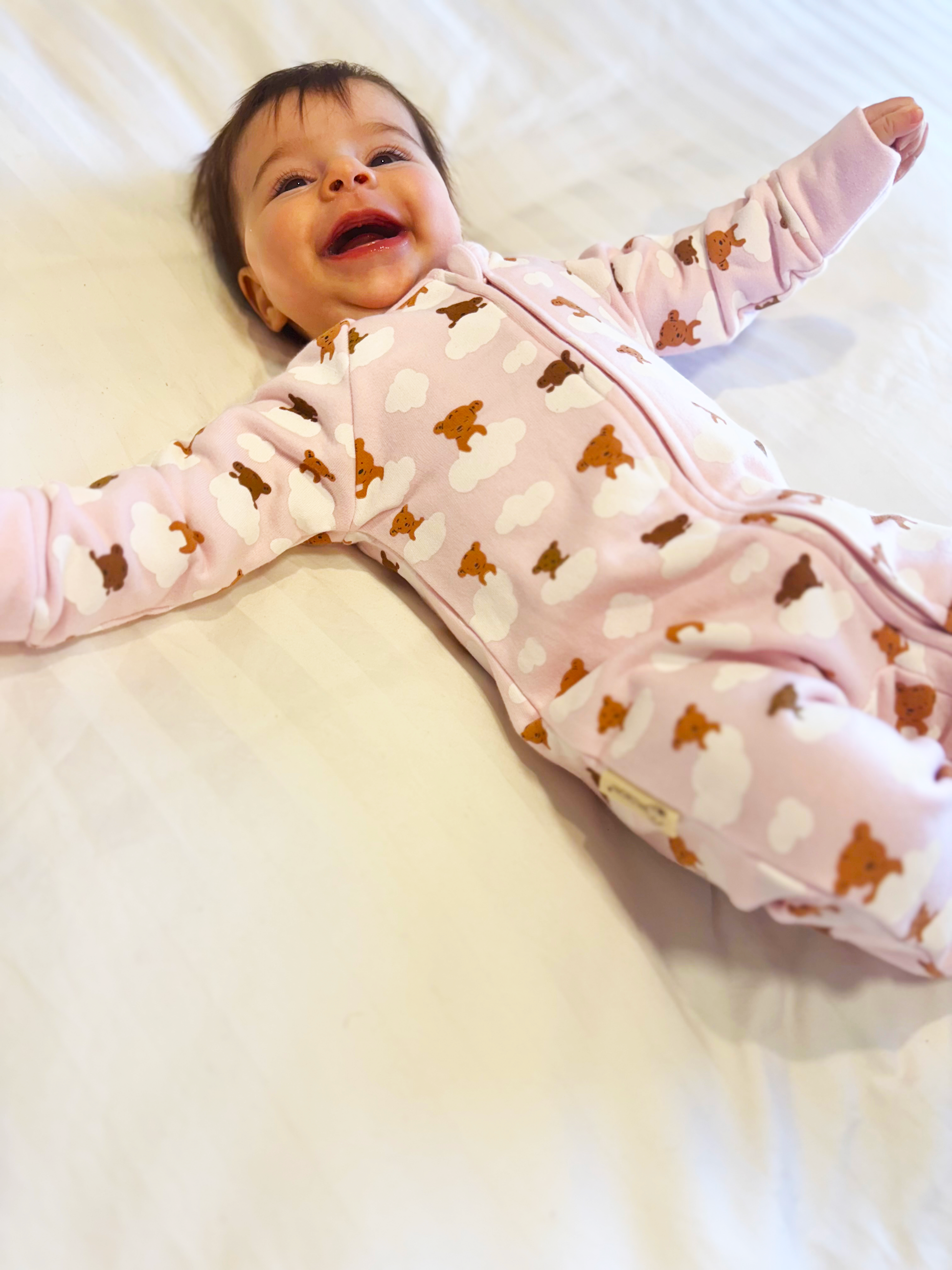 Baby in a pink outfit with brown bear patterns lying on a white surface